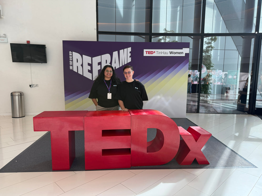 Two ACS founders standing behind a large red TEDx sign in front of the TEDxTinHauWomen ‘Reframe’ backdrop.