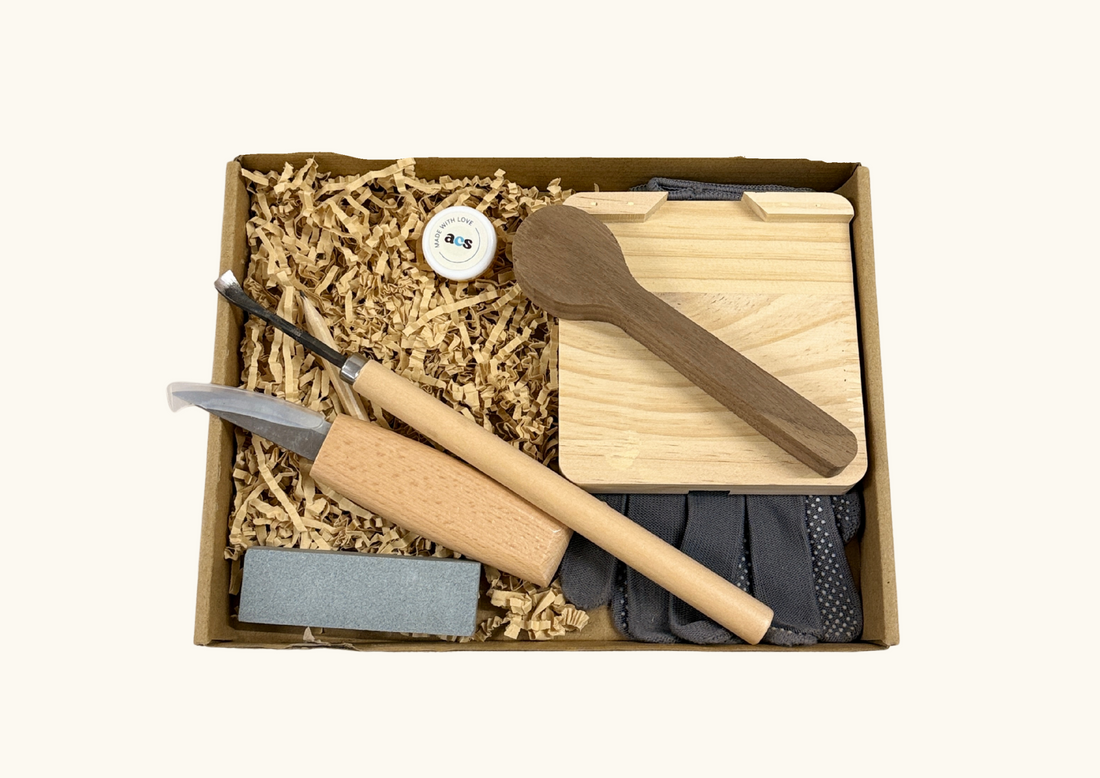 Spoon carving kit in a box with tools, wooden board, and a finished carved wooden spoon.