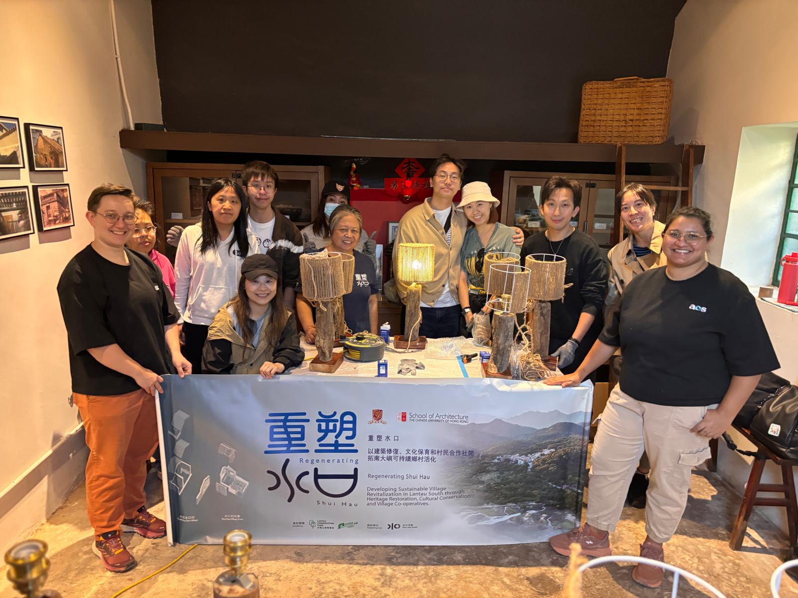 Group of people posing in front of a banner for CUHK School of Architecture's Regenerating Shui Hau Driftwood Lamp making workshop by a collective space
