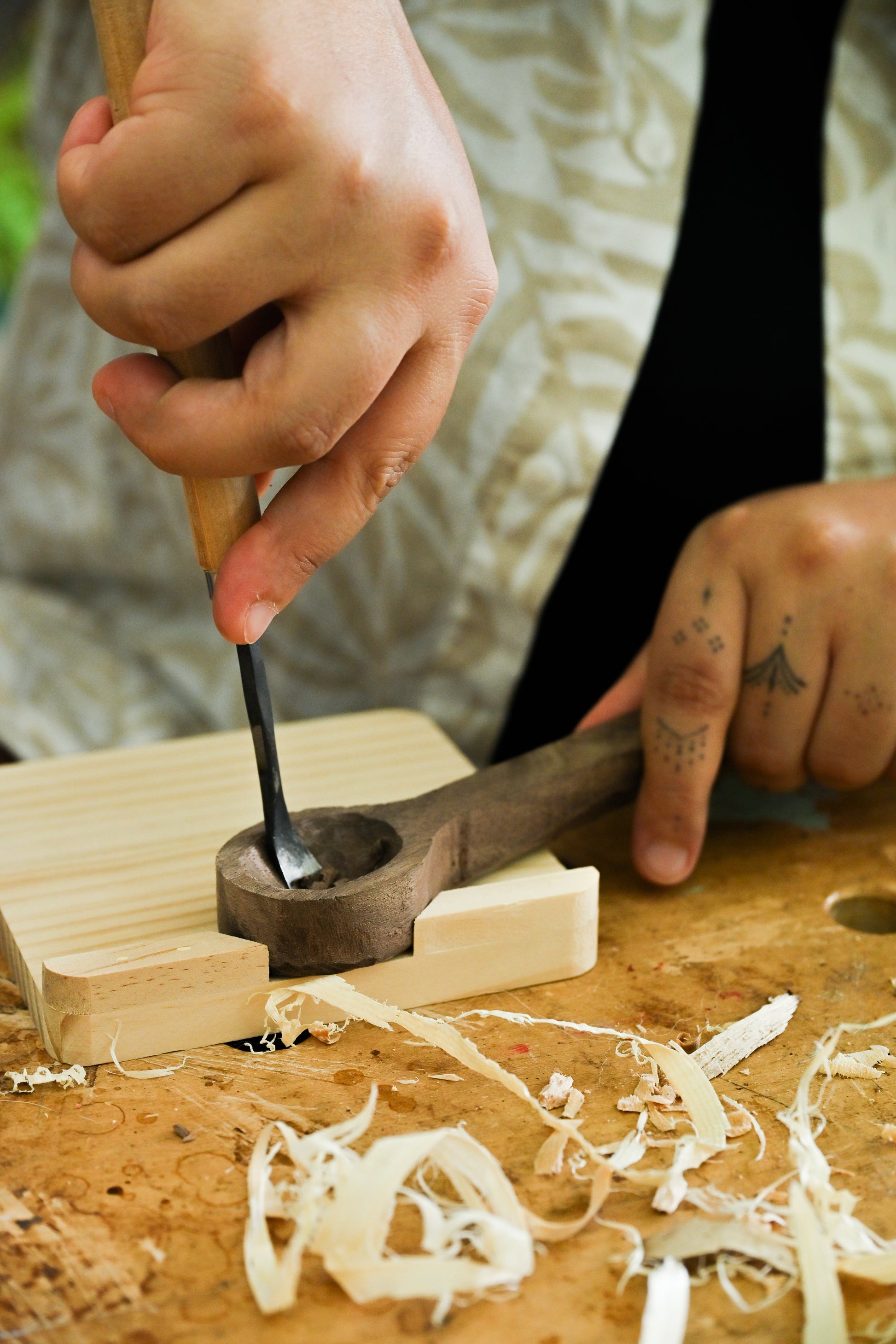 Participant carving a wooden spoon handle with a chisel on a workbench, with wood shavings scattered around.