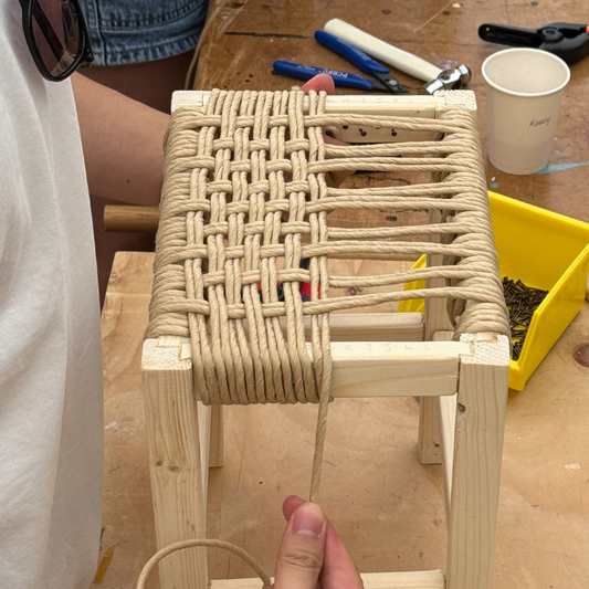 Hands weaving a Danish cord stool seat.