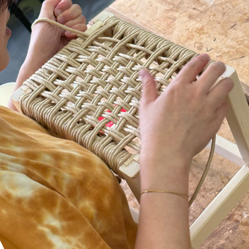 Close-up of Danish cord weaving on a wooden stool frame.