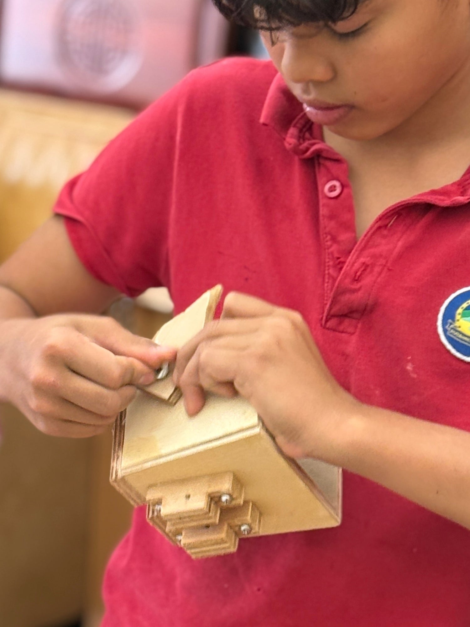 Child in a red shirt working on a wooden project at a table