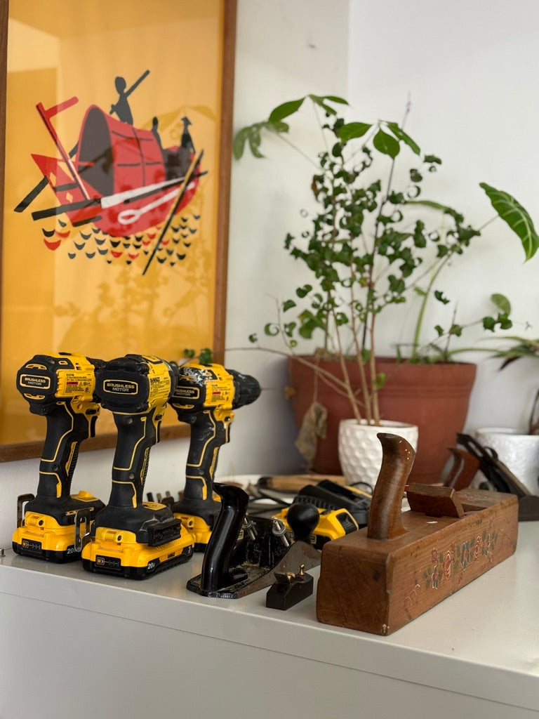 Set of power drills on a shelf with decorative items in the background