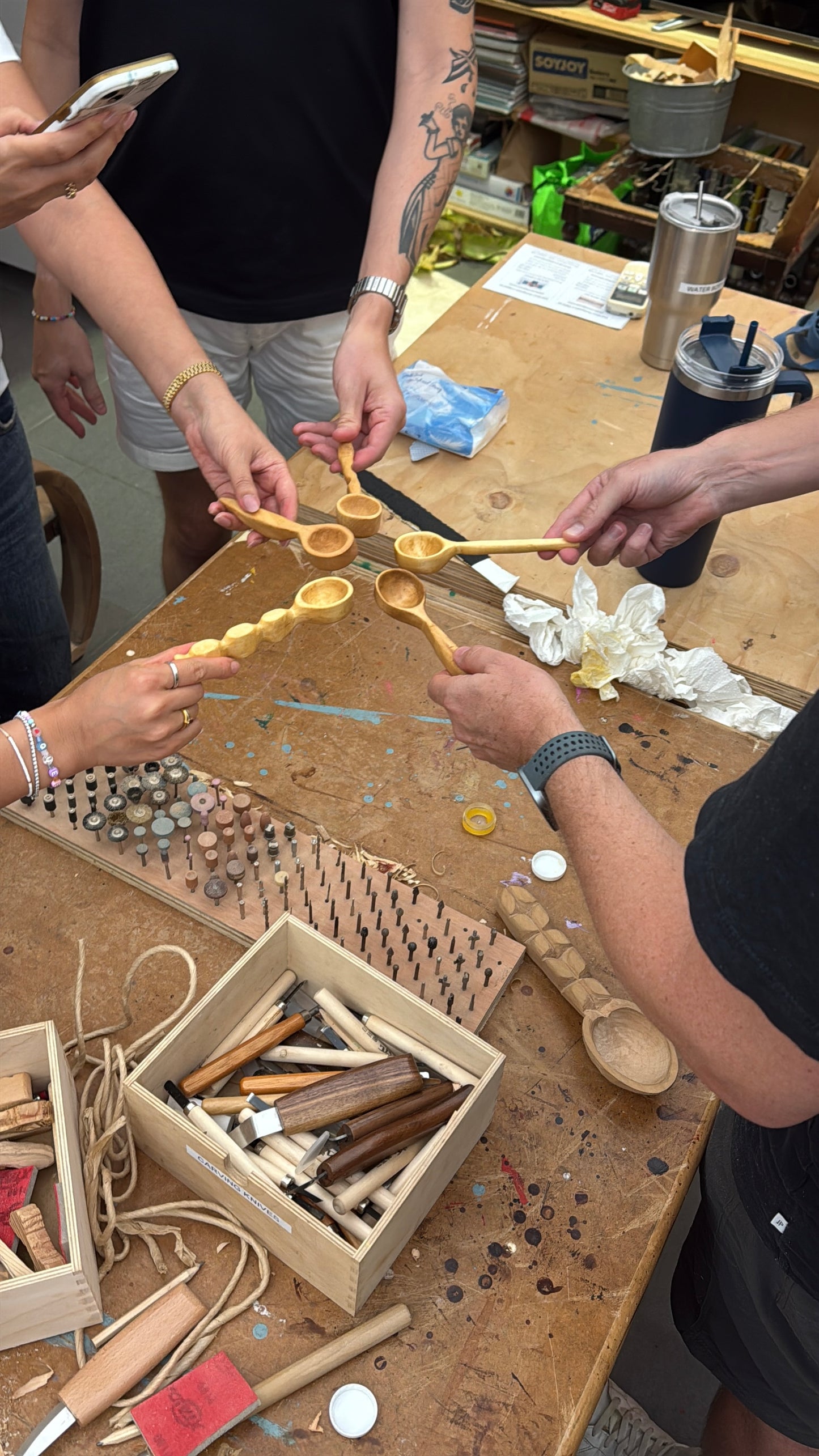 Participants carving wooden spoons at a workshop table.